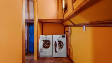 A laundry room with two front-loading washing machines, wooden floors, and yellow walls.