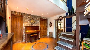 Una habitació àmplia amb paret de maó, portes de fusta, un piano i una escala amb sòl estampat.
