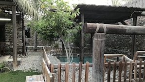 A wooden deck with a pool, surrounded by a wooden fence and stone walls. - Among the Mountains (Mirbah)