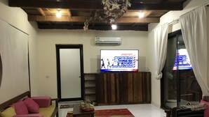 A living room with a sofa, a coffee table, a TV on a wooden stand, and a colorful striped rug. - Among the Mountains (Mirbah)
