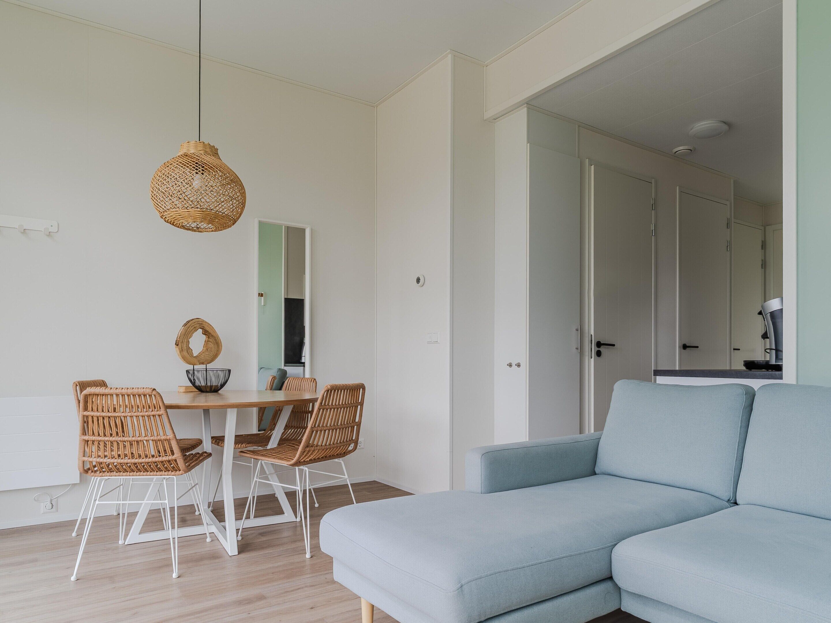 Una sala moderna con un sofá azul claro, una mesa de comedor con sillas de mimbre y una lámpara colgante.