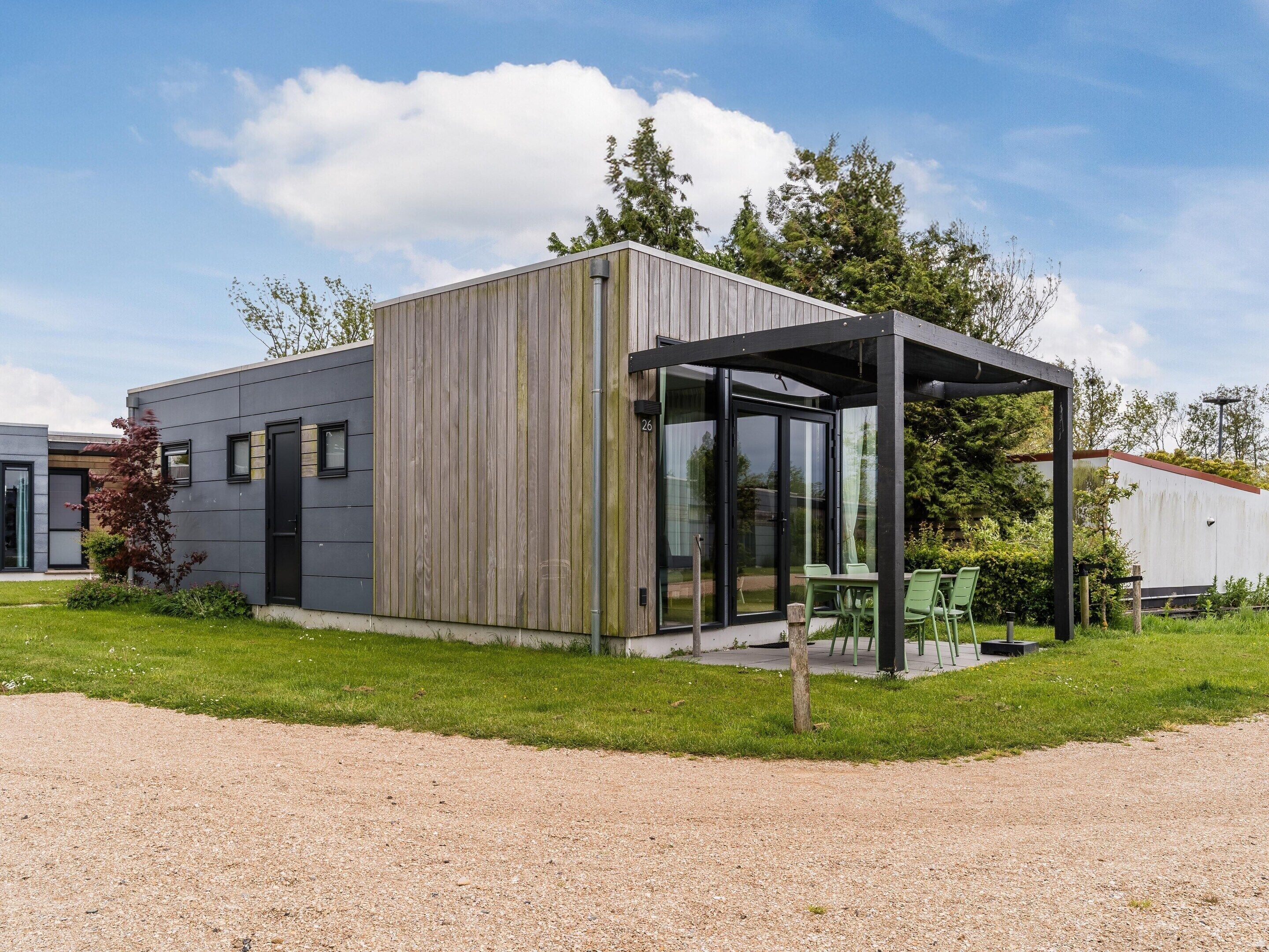 A modern building with a covered outdoor seating area, a gravel driveway, and surrounding greenery.