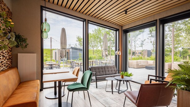 Un intérieur moderne avec un plafond en bois, de grandes fenêtres et différents types de sièges, notamment un canapé, des fauteuils et une table.