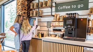 L’intérieur d’un café, avec un menu numérique, du matériel pour préparer le café et un panneau indiquant « Café à emporter ».
