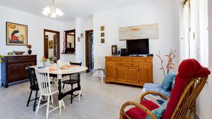 A dining area with a round table, chairs, and a television on a wooden cabinet. - Beachfront Villa With Solarium (Siniscola)