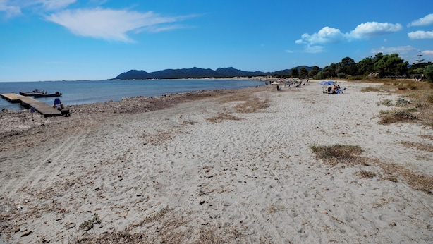 A beach with a wooden pier, boats, and people relaxing under umbrellas. - Beachfront Villa With Solarium (Siniscola)