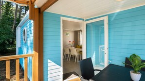 A covered outdoor seating area with a table and chairs, a potted plant, and a view of the interior through an open door. - Neat Chalet With Microwave, Near Antwerp (Rijkevorsel)