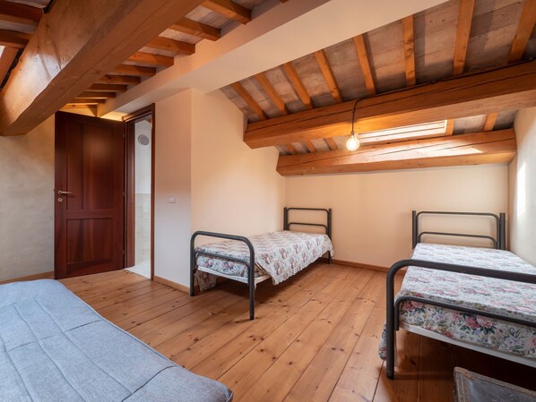 A small, cozy room with wooden floors and a sloped ceiling. There are two metal beds with floral bedding and a single sofa. - Holiday Home in Villagrande Near Pool & Beach (Mombaroccio)