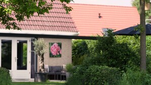 A house with a red roof, a garden with a lawn, and a patio area with outdoor furniture. - Vacation Home With Jacuzzi (Schoonloo)