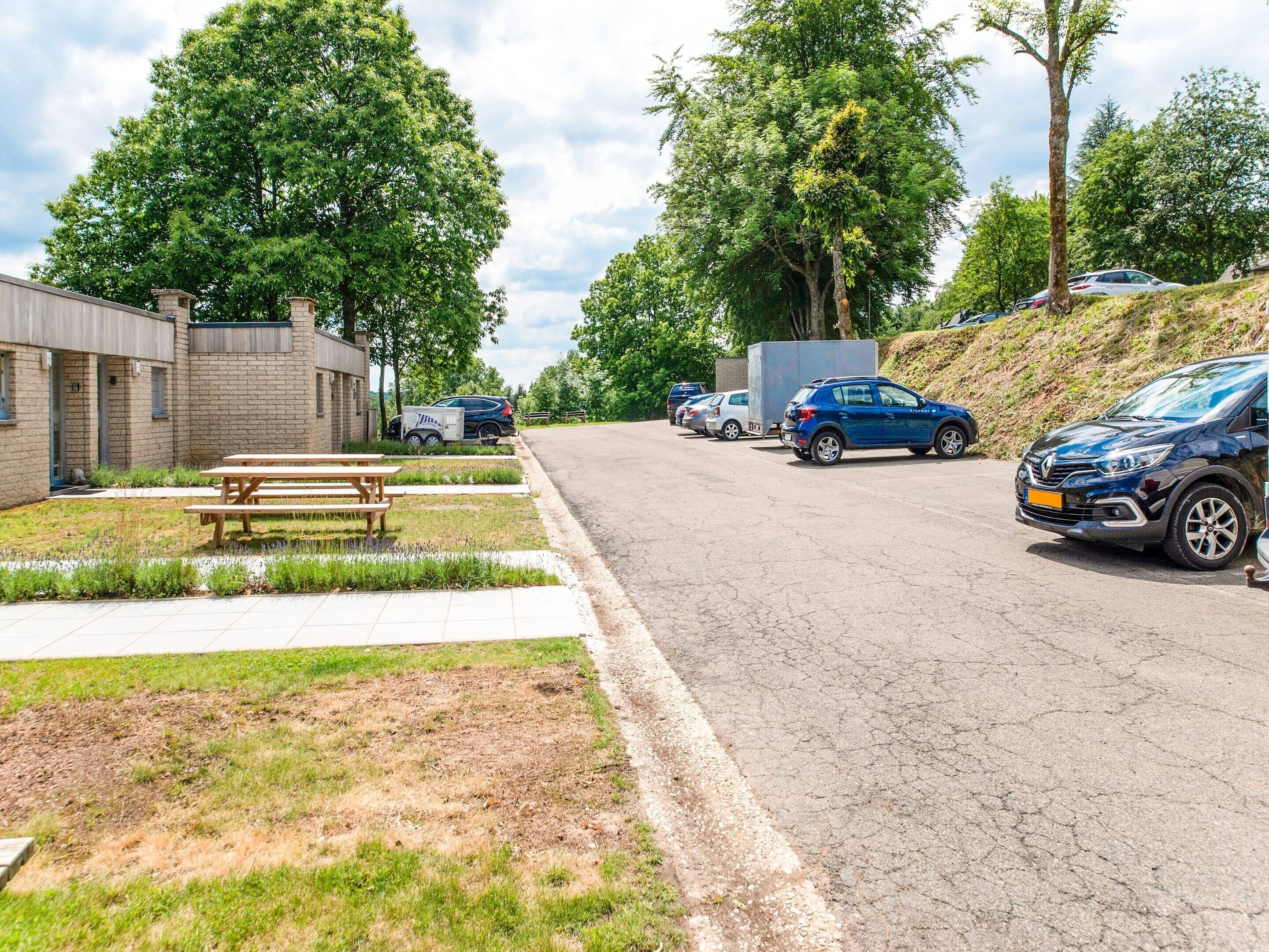 Un parking avec des voitures, des tables de pique-nique et un bâtiment aux murs en briques.