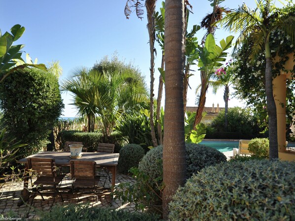 Eine Terrasse mit Tisch und Stühlen, umgeben von üppiger Bepflanzung und einem Schwimmbecken.