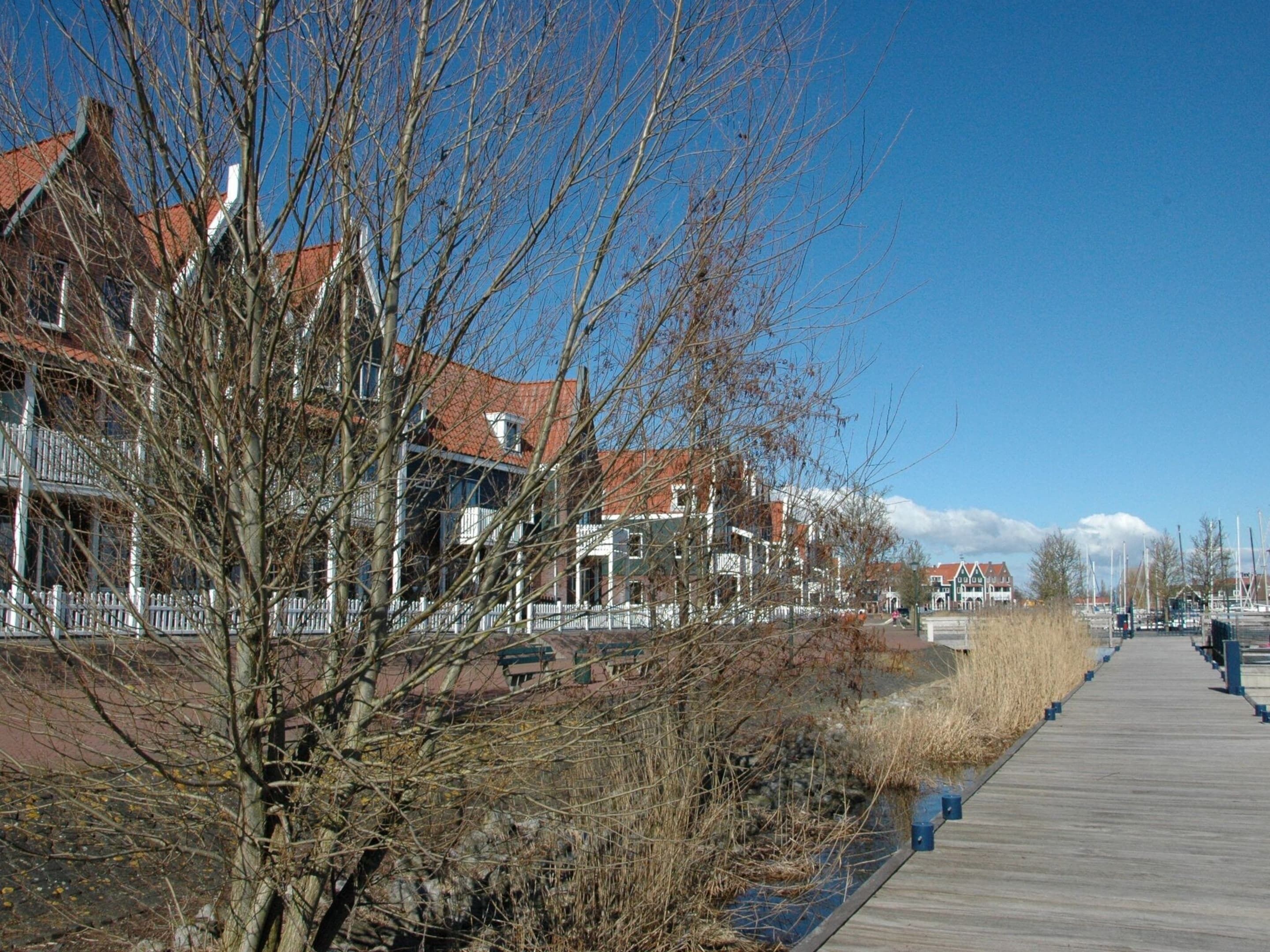 Un muelle de madera con edificios a un lado y un puerto deportivo al otro.