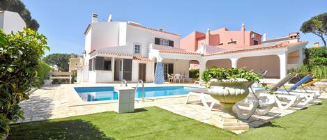 A modern house with a swimming pool, outdoor seating, and a well-maintained lawn.