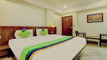A hotel room with a large bed, a wooden headboard, a desk, a chair, and a painting on the wall.