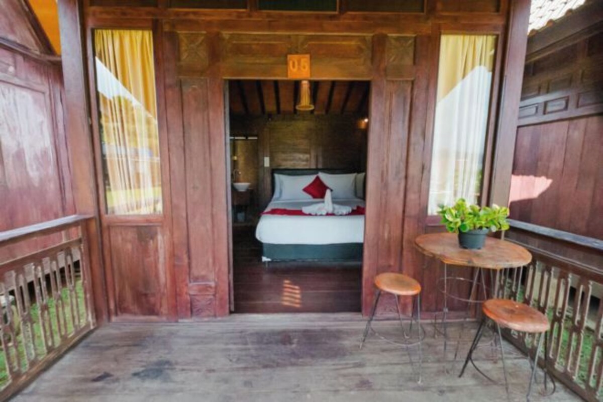 Une pièce en bois avec un lit, une petite table sur laquelle est posée une plante, et une chaise.