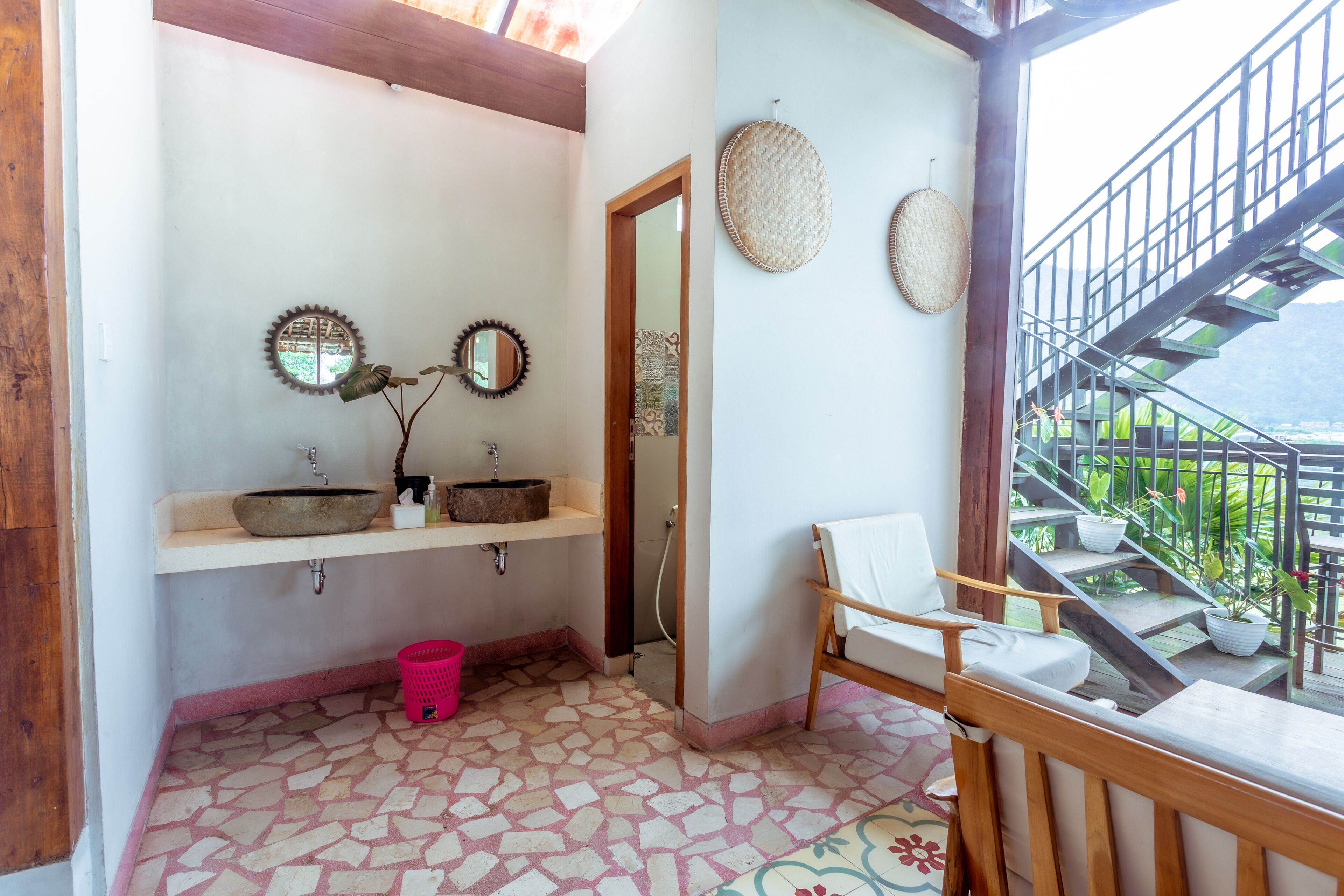 A bathroom with two sinks, a shower, a chair, and a staircase leading to an outdoor area.