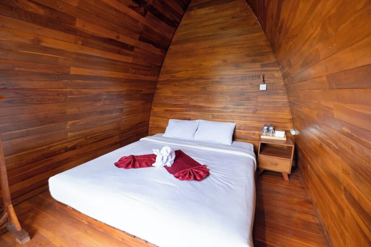 A wooden-paneled room with a bed, pillows, a nightstand, and a small table with items on it.