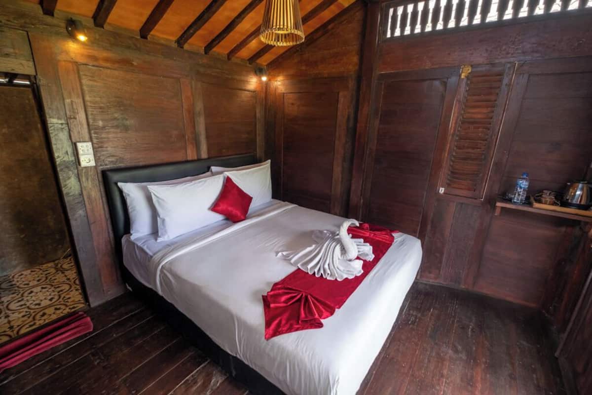 A wooden room with a bed, a red throw, and a towel arrangement.