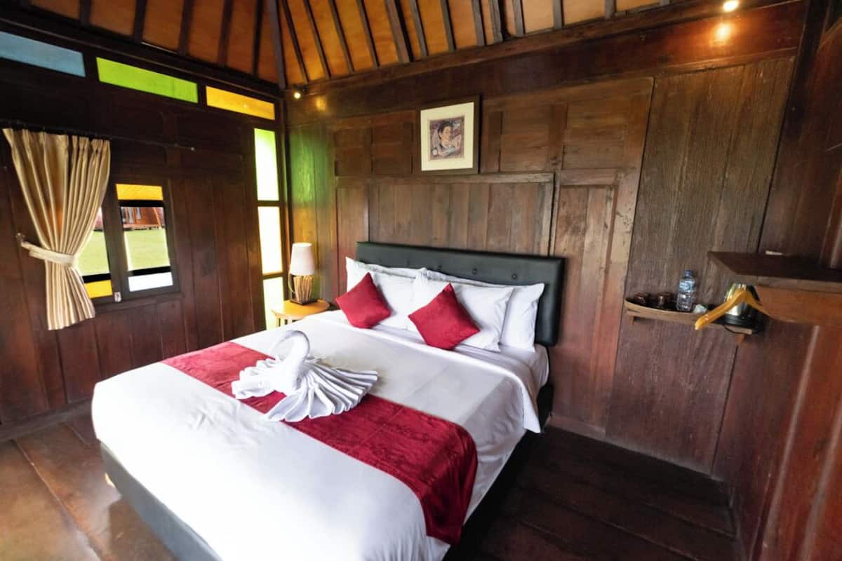 A neatly made bed with red and white linens, a wooden headboard, and a framed picture on the wall.
