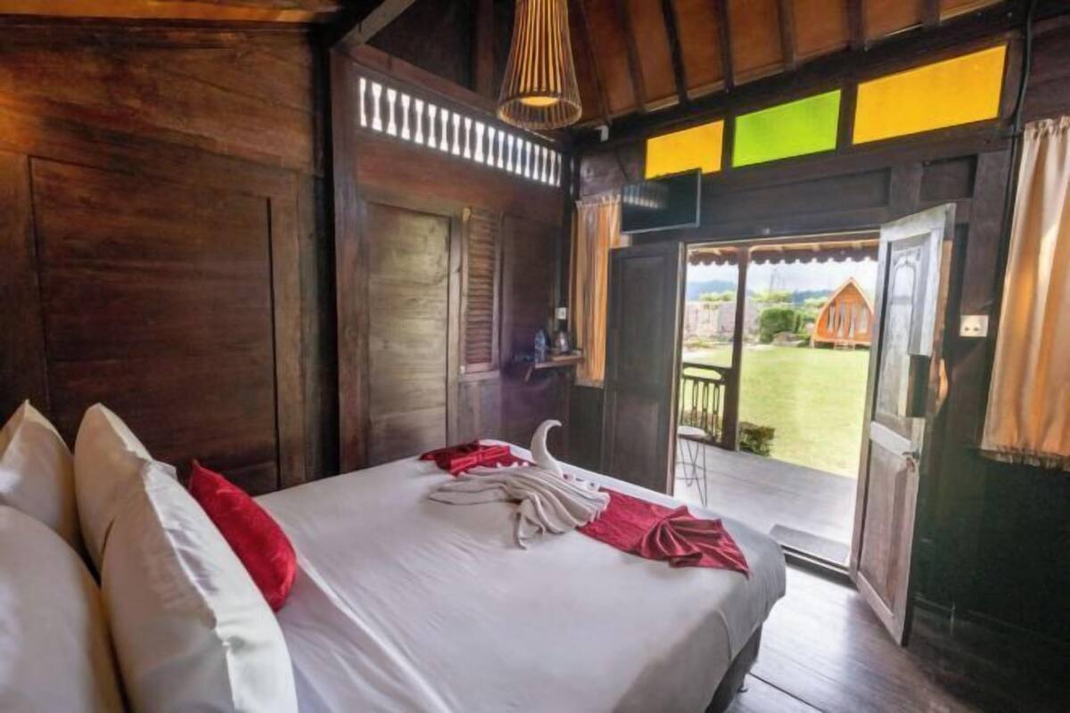 A wooden room with a bed, a hanging light fixture, and a door leading outside.