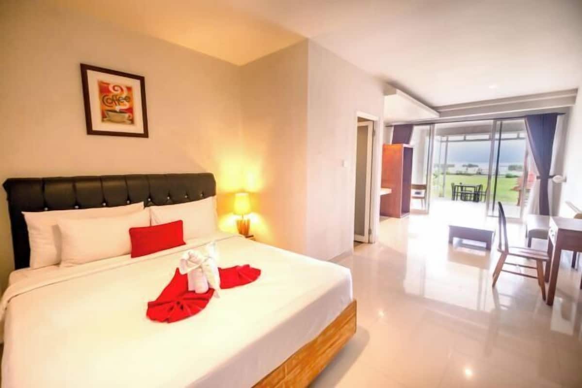 A hotel room with a bed, a nightstand, a lamp, a framed picture on the wall, and a view of the outdoors.