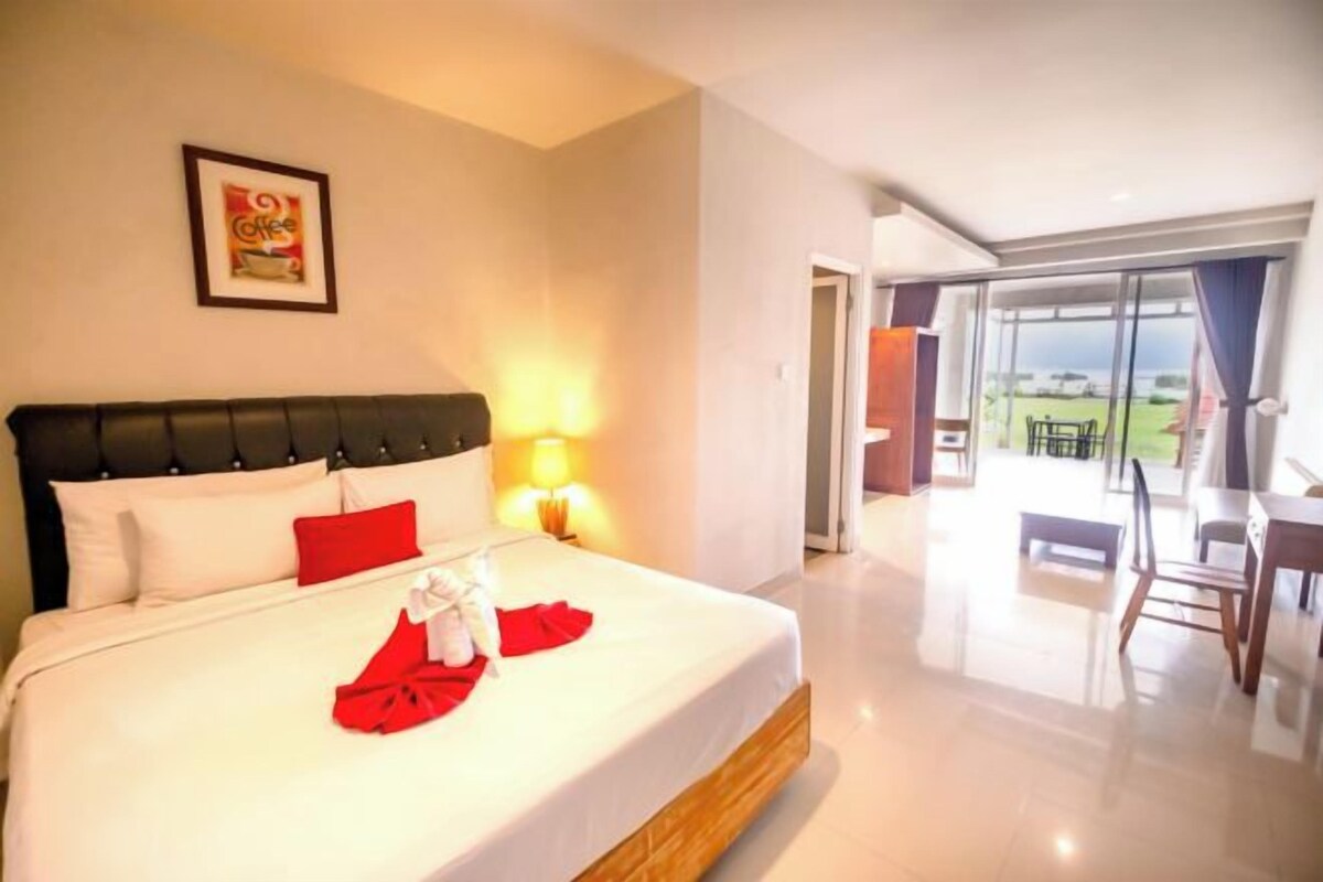 Una habitación de hotel con cama, mesita de noche, lámpara, un cuadro en la pared y vistas al exterior.