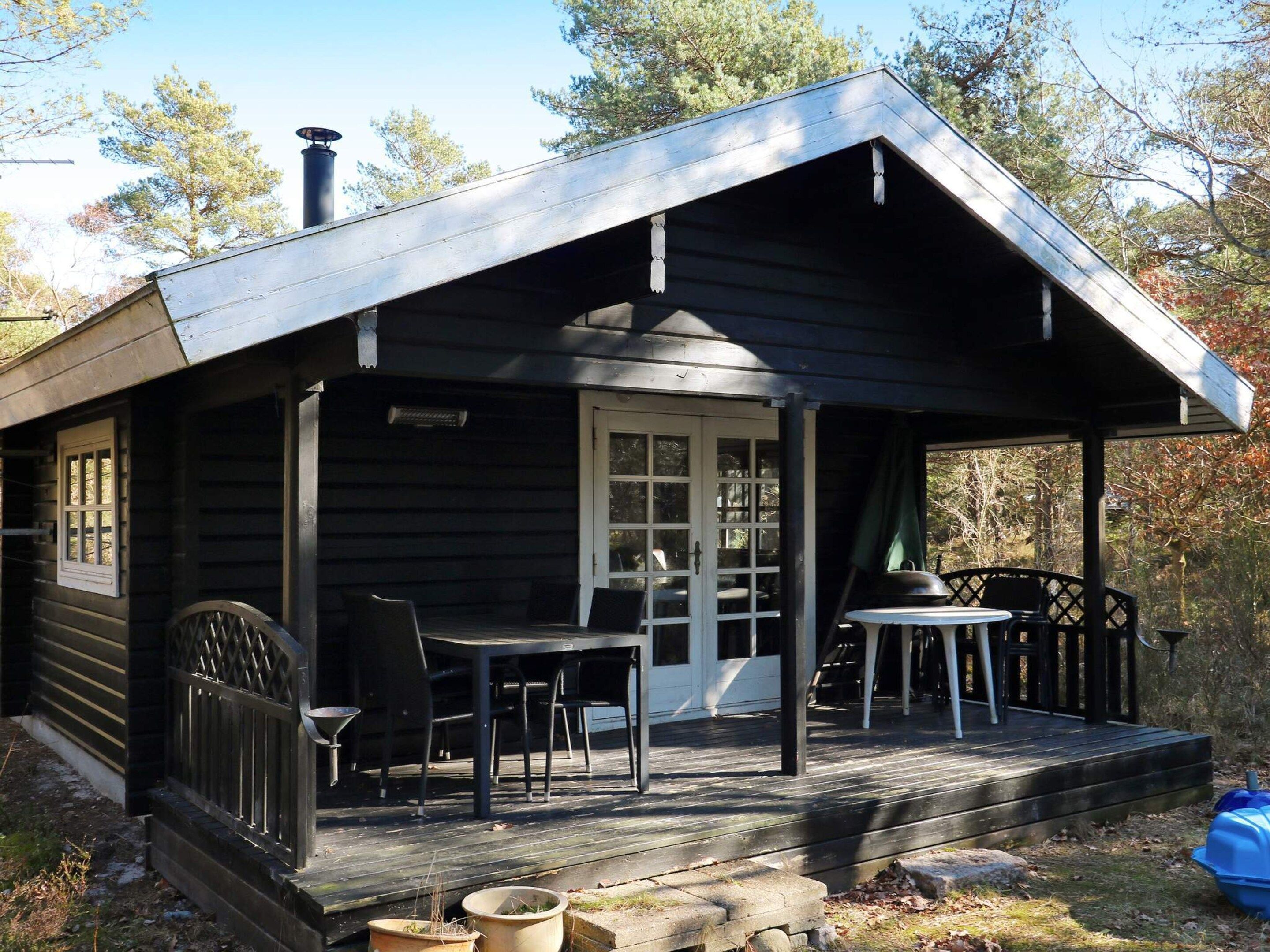A wooden cabin with a porch, a table, and chairs.