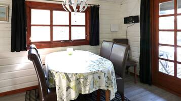 A dining area with a round table, two chairs, a chandelier, and large windows with curtains.