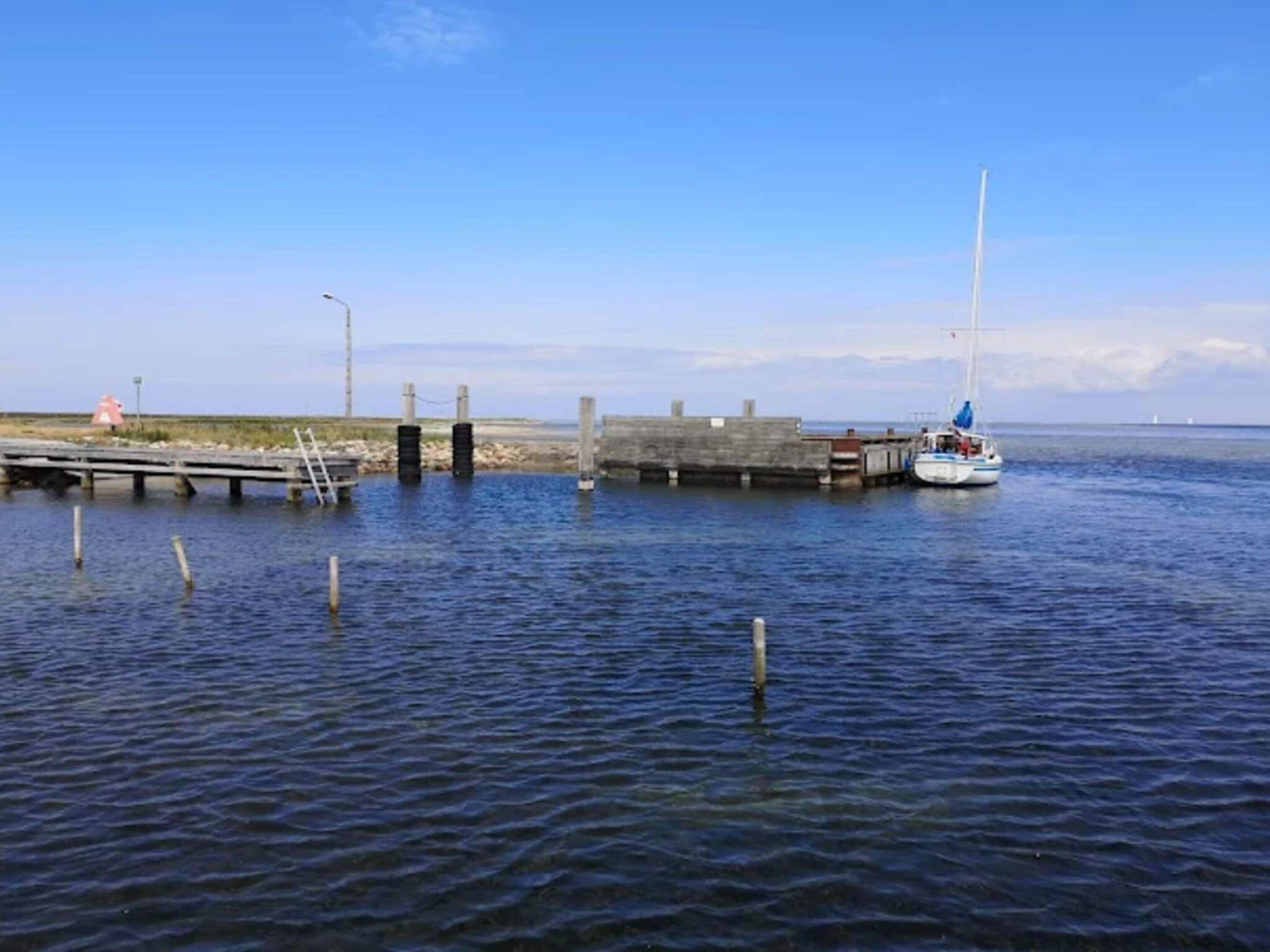 A pier extending into calm waters with a sailboat docked at the end.