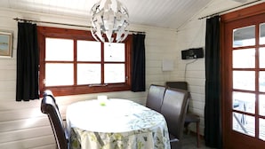 Un coin repas avec une table ronde, deux chaises, un lustre et de grandes fenêtres avec des rideaux.