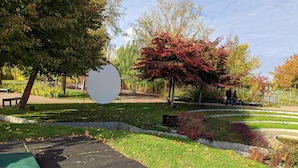 Ein Park mit einer runden Aussichtsplattform, einem gepflasterten Weg und verschiedenen Bäumen, darunter ein Baum mit roten Blättern.