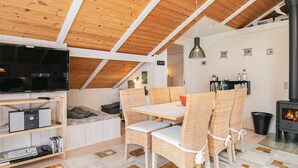Une chambre à coucher confortable aménagée en mezzanine, avec un plafond en pente, une télévision, une bibliothèque, une table à manger entourée de chaises en osier et une cheminée.