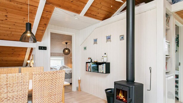 Une pièce chaleureuse avec un plafond en bois, un poêle à bois noir, une bibliothèque et un fauteuil en osier.