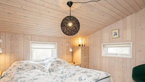 Une chambre à coucher avec un lit, des murs en bois, un luminaire suspendu, une commode et une chaise.