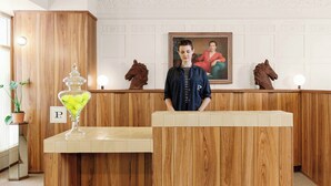 A reception desk with a wooden finish, a potted plant, a glass container with yellow items, and a framed portrait on the wall.