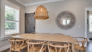 Ein Esszimmer mit einem großen Holztisch, sechs Stühlen, einer Hängelampe und einem dekorativen Spiegel an der Wand.