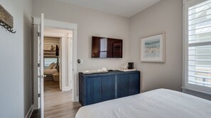 Un dormitorio con cama, cómoda, televisor y ventana con persianas.