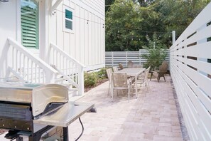 En uteplats med ett bord och stolar, en grill och ett vitt staket.