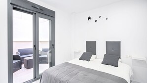 Une chambre moderne avec un grand lit, une porte-fenêtre coulissante donnant sur un espace extérieur aménagé, et une décoration minimaliste.