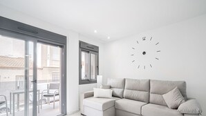 Un salon moderne avec un canapé d’angle gris, une petite table d’appoint grise et une grande horloge murale.
