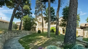 A stone pathway leading to a building with a stone facade, surrounded by trees and a well-maintained lawn with purple flowers. - Apartment in Noble Villa Near Ecological Park (Mombaroccio)