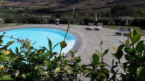 A swimming pool with lounge chairs and an umbrella, surrounded by a brick patio. - Apartment in Noble Villa Near Ecological Park (Mombaroccio)