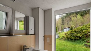 A modern bathroom with a large sink, a mirror, and a view of a green garden through a glass door. - Home in Steinbach-hallenberg (Steinbach-Hallenberg)