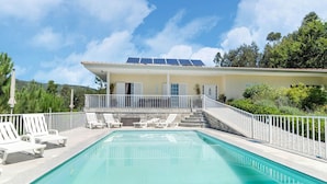 Ein Swimmingpool mit Liegestühlen, einem weißen Zaun und einem Gebäude mit Solaranlage.