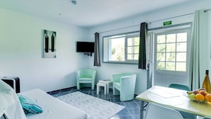 Ein Hotelzimmer mit Bett, zwei Stühlen, einem kleinen Tisch mit Obst, einem Fernseher und einem Fenster mit Vorhängen.