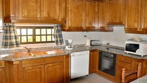 Una cocina con armarios de madera, lavavajillas, horno, microondas y ventana con cortina de cuadros.