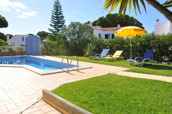Une piscine dotée d’une terrasse carrelée, entourée de pelouse et d’arbres.