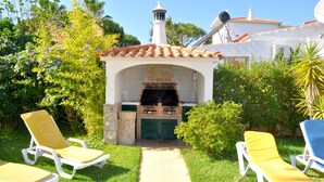 Un patio con una chimenea de ladrillo, dos sillones de descanso y un sendero que conduce a él.