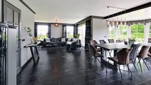 A spacious room with a large dining table, comfortable seating, and large windows offering a view of greenery. - Tasteful Villa in Didam With Garden (Didam)