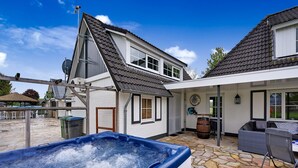 A hot tub in a backyard with stone flooring, a covered patio area, and a house with a sloped roof. - Tasteful Villa in Didam With Garden (Didam)
